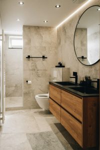 Baño remodelado con espejo redondo y mueble de madera