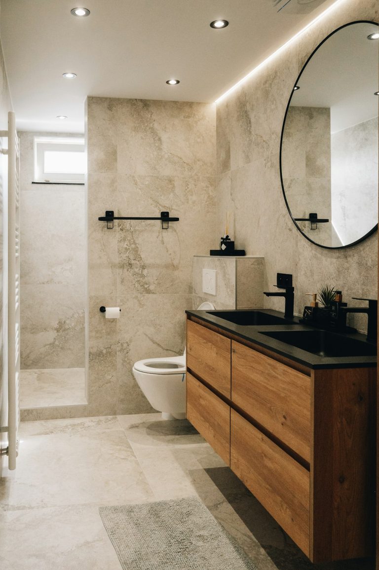 Baño remodelado con espejo redondo y mueble de madera